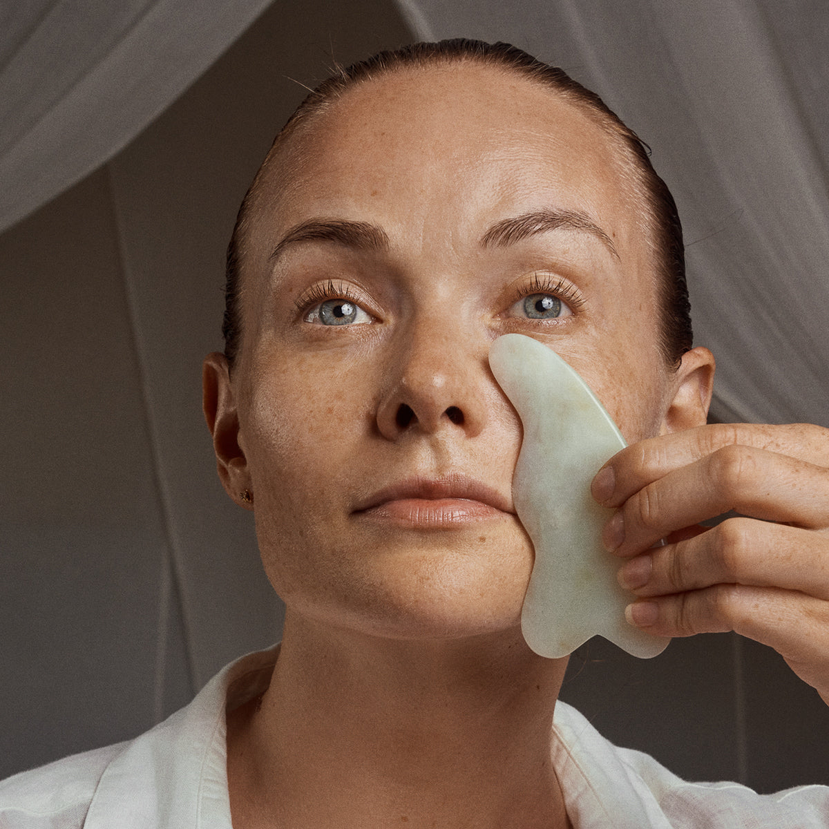 Person using a gua sha tool on their face with a neutral background