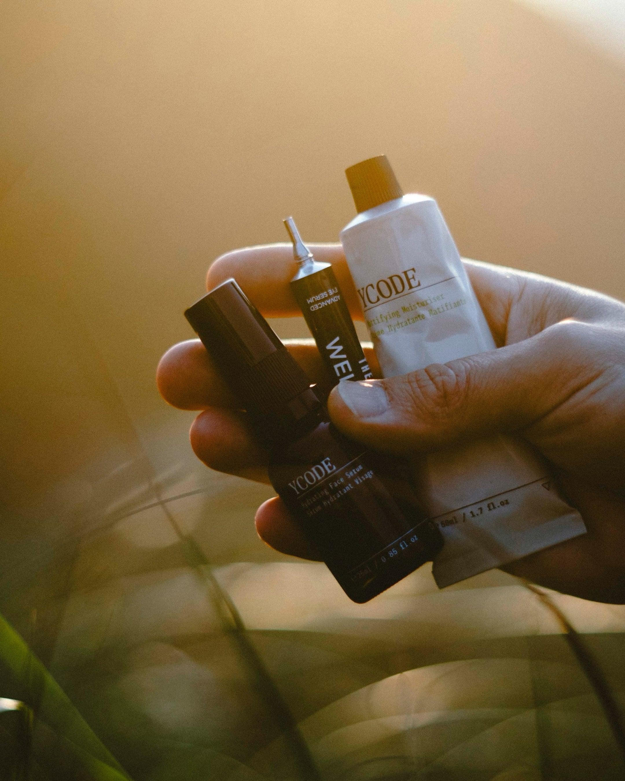 Hand holding three skincare bottles with a blurred natural background